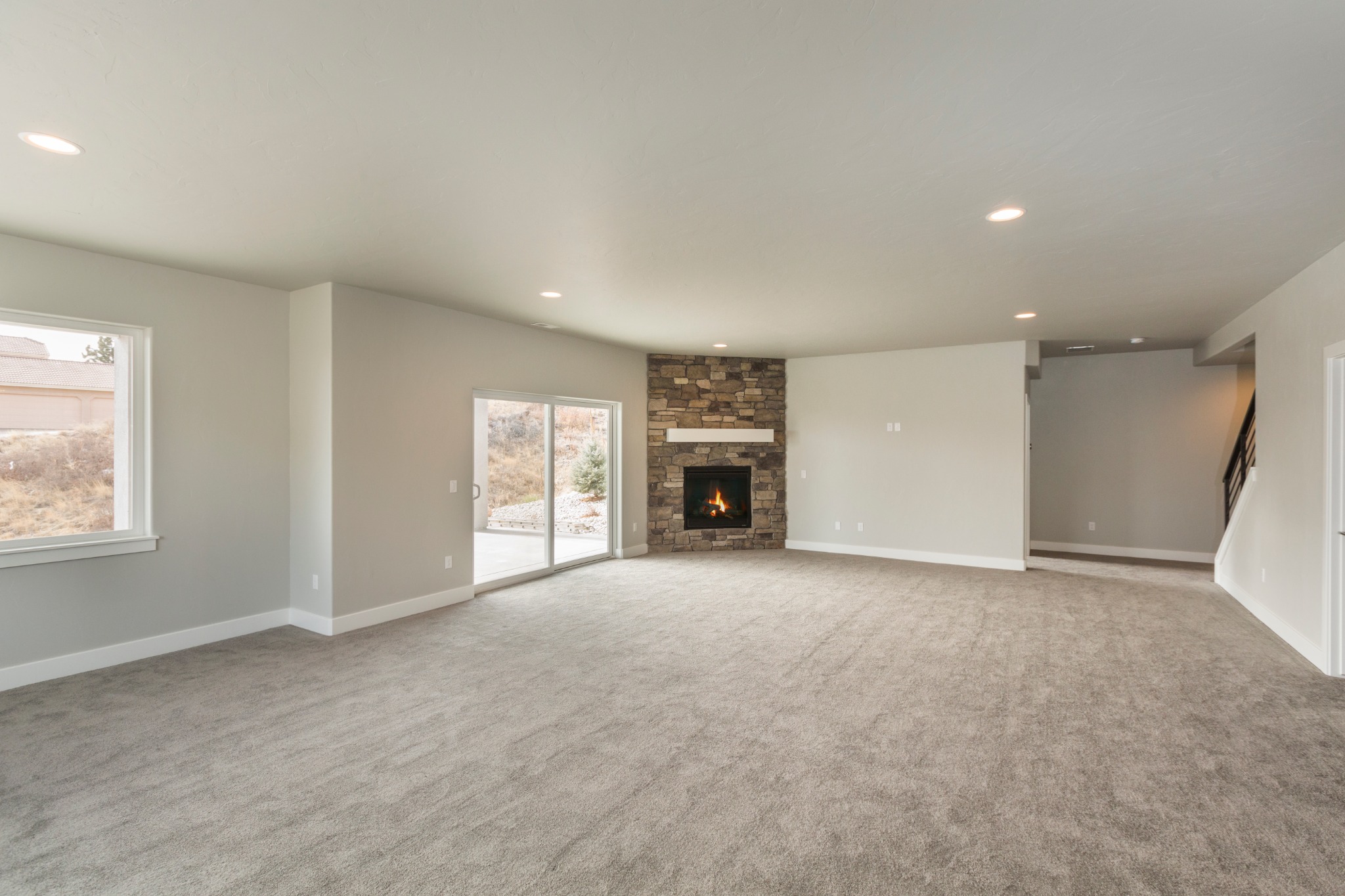 Spacious basement with gray carpet, stone fireplace, recessed lighting, and sliding glass doors providing natural light and access to the outdoor patio.