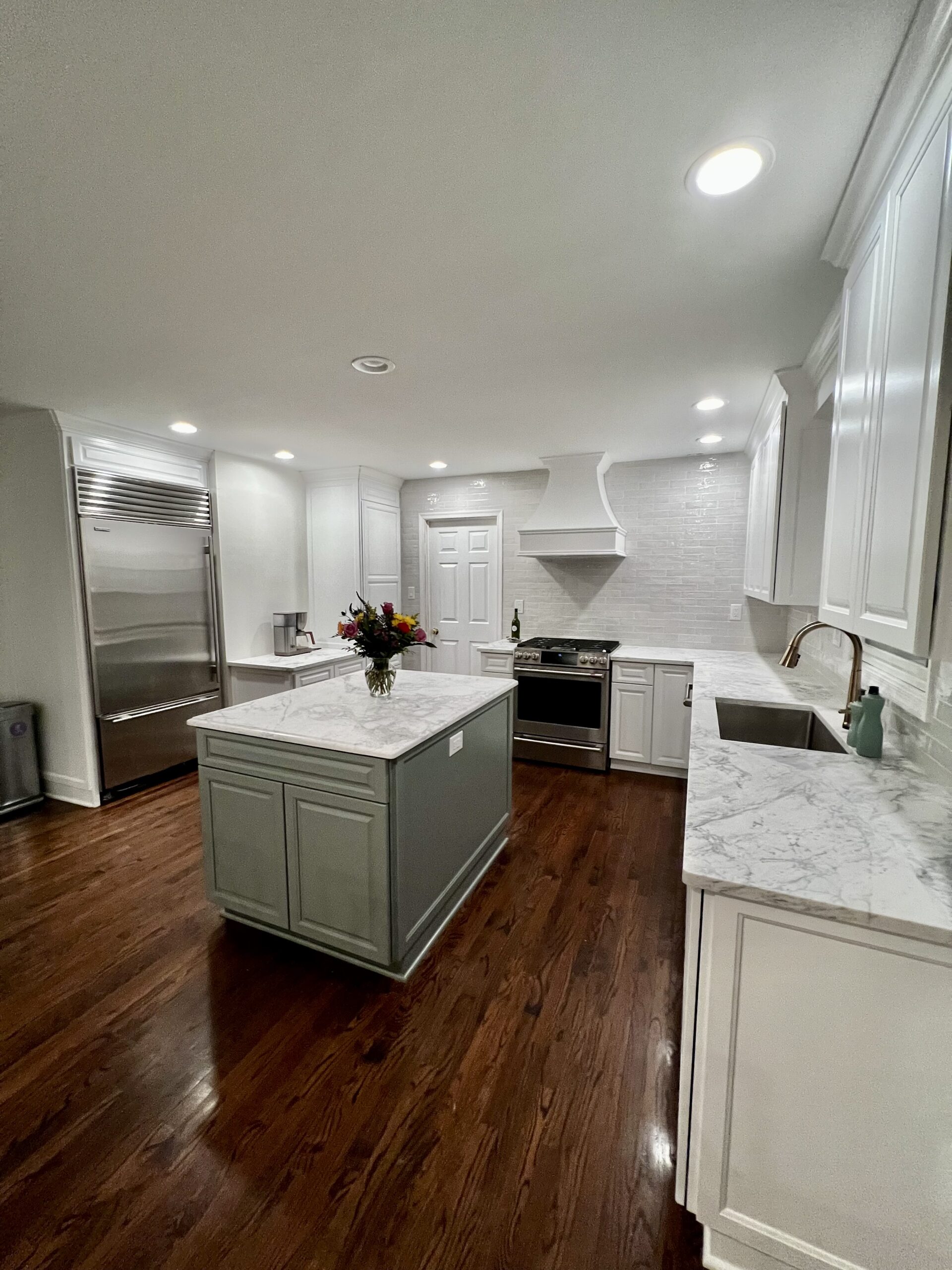 Bright kitchen with marble countertops, white cabinetry, stainless steel appliances, a gray island centerpiece, and dark hardwood floors.