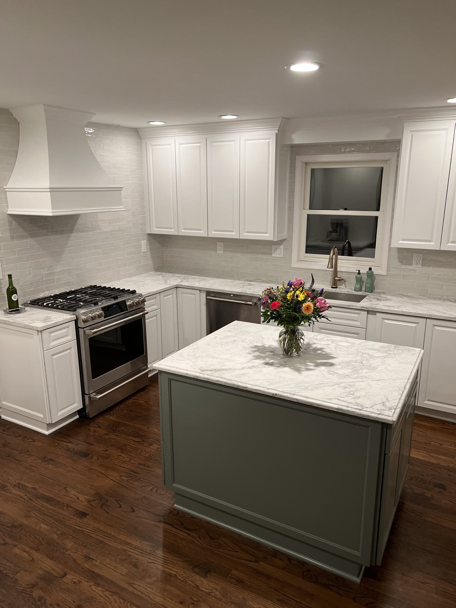 Bright kitchen with white cabinetry, marble countertops, a gray island, stainless steel appliances, subway tile backsplash, and dark hardwood floors.