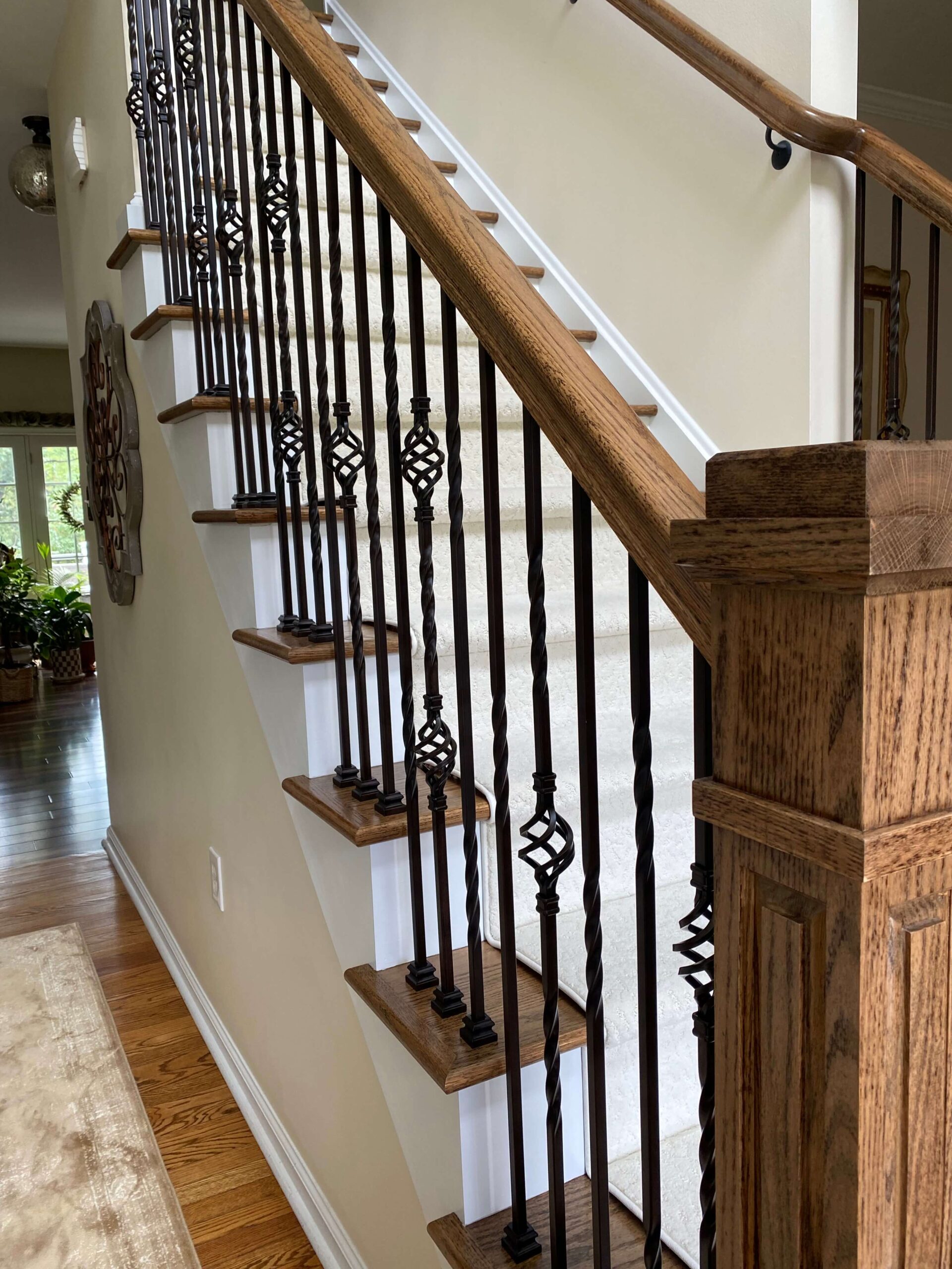 Wood staircase with dark wood handrail and newel post, featuring black wrought iron balusters with decorative twists and knuckles, and carpeted stair treads.