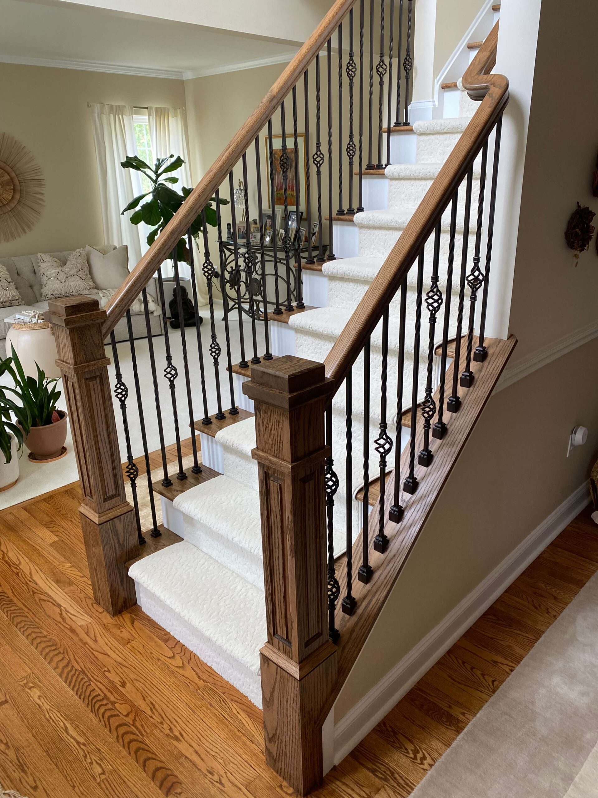 Wood staircase with white risers, carpeted steps, dark iron balusters featuring decorative twists, and a wooden handrail, leading into a cozy living area.