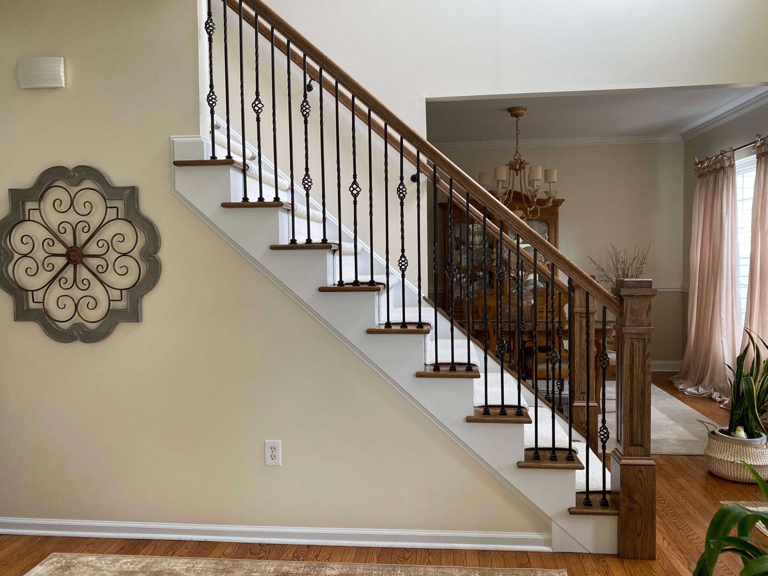 Wood staircase with white risers, dark wood treads, black wrought iron balusters with decorative twists, and a wooden handrail next to a dining room.