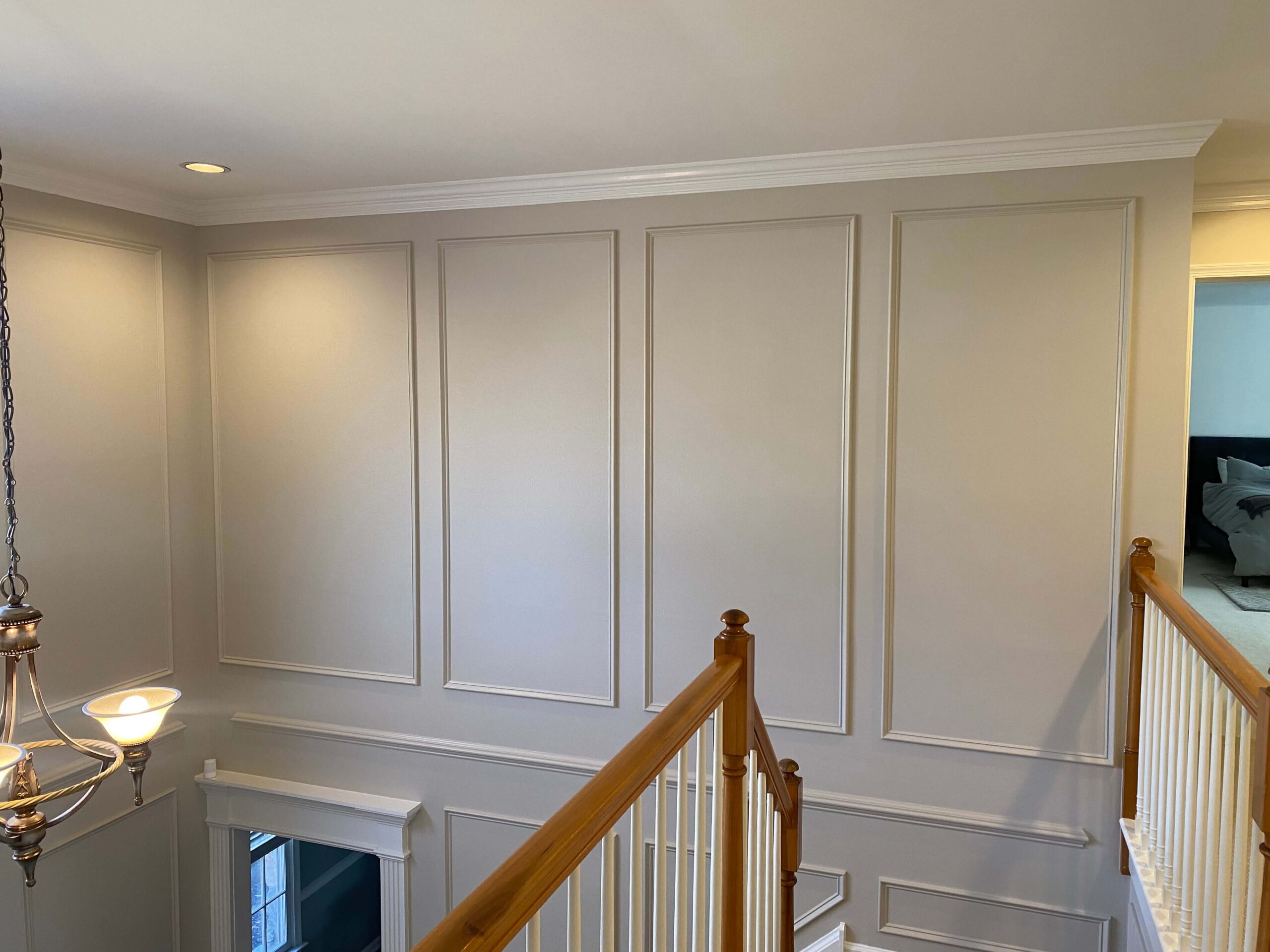 Second-floor hallway with beige paneled walls, white crown molding, a wooden railing with white balusters, and a hanging light fixture above the stairs.